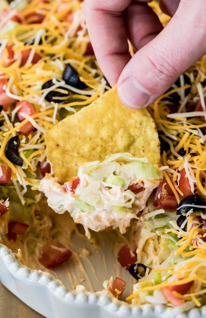 The BEST, easiest Taco Dip! This is so easy to make and so good! #tacodip #recipe #dip #cookout #summerfood scooping taco dip onto a chip