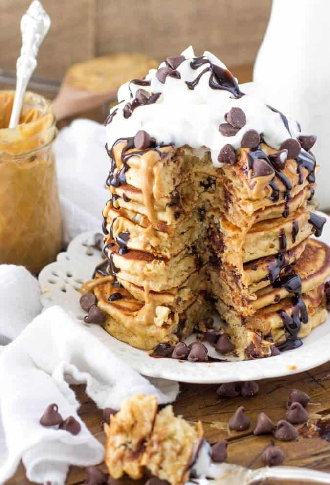 Tall stack of Stack of peanut butter chocolate chip pancakes, drizzled with chocolate sauce and topped with whipped cream and chocolate chips