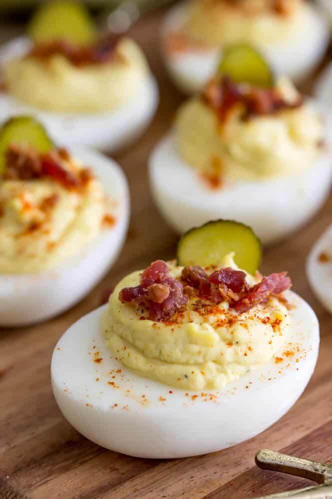 Simply the best deviled eggs recipe! This recipe uses a secret ingredient and they are so good! #deviledeggs #easterrecipe Deviled eggs topped off with paprika, bacon, and sweet pickle slices