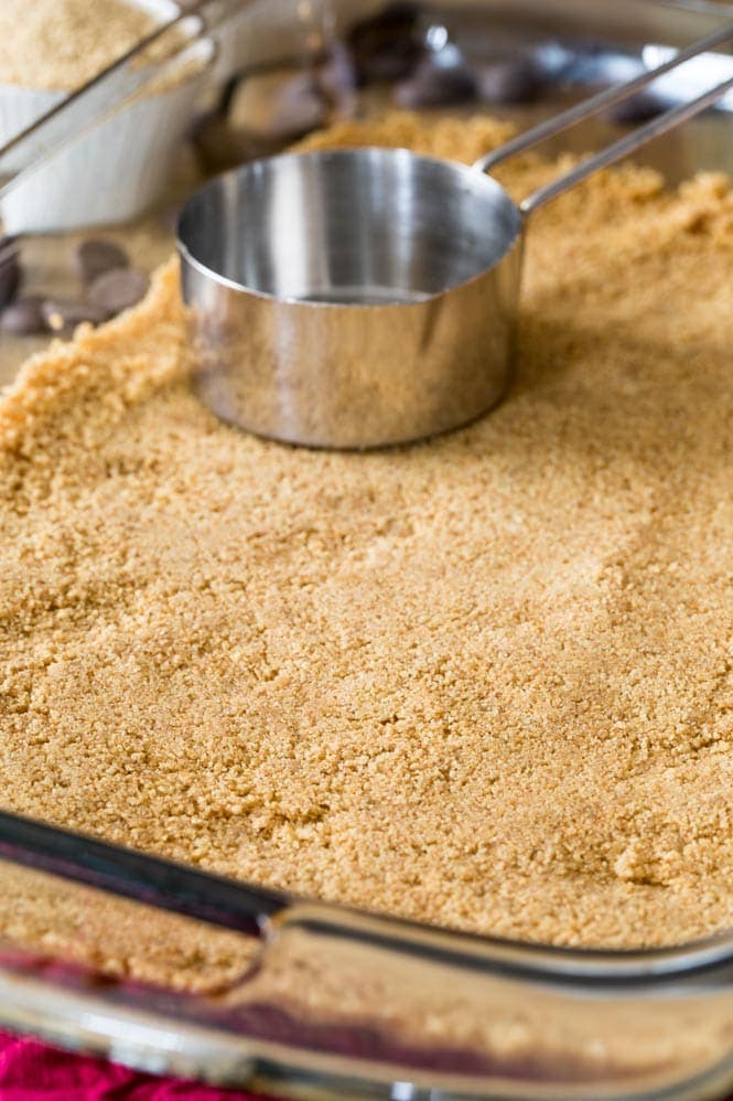 The first layer of 7 Layer Bars Showing how to make a graham cracker crust for Magic Cookie Bars