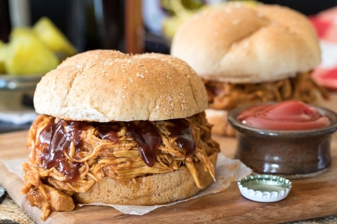 This is the BEST BBQ Chicken I've ever tasted! #bbqchicken #recipe BBQ Pulled Chicken sandwich on a wooden platter beside a ketchup dish