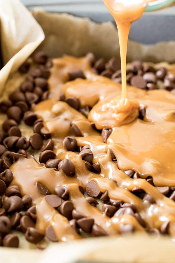 OMG these Carmelitas are amazing! Chewy, melty, caramel and chocolate filling encased in a buttery crisp cookie layer, these are a MUST try! #cookiebars #carmelitas #partyfood #bestdessert #easyrecipe Pouring melted caramel over chocolate chips for carmelitas