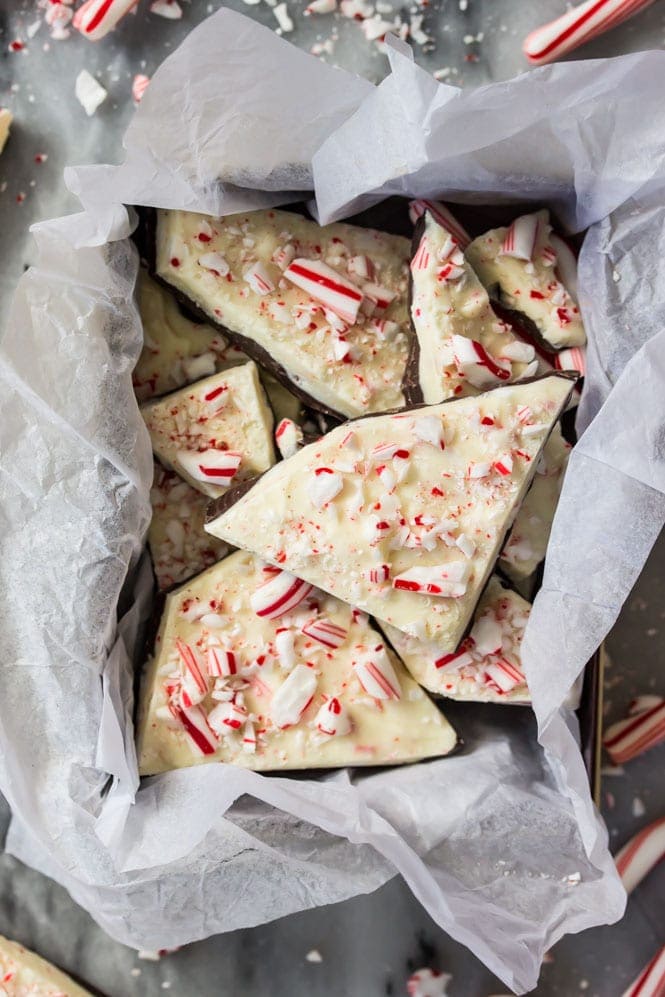 How to make an easy PEPPERMINT BARK at home! Super simple and SO good! #christmascandy #peppermintbark Peppermint Bark pieces in container on marble surface