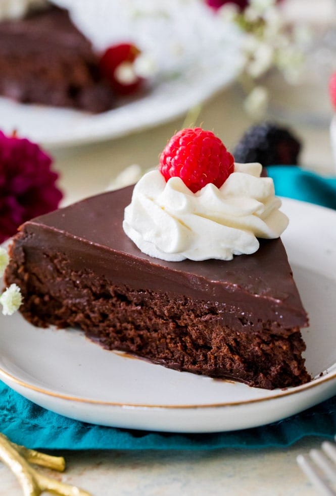 A rich, dense, & supremely fudgy FLOURLESS CHOCOLATE CAKE! #flourlesschocolatecake #glutenfree Slice of flourless chocolate cake on white plate