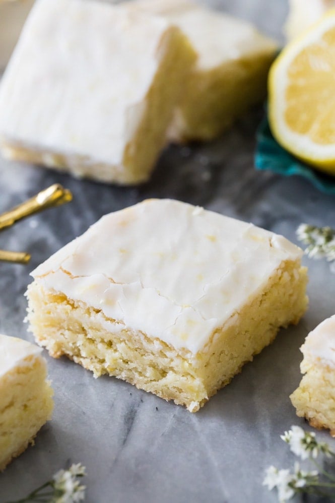 These LEMON BROWNIES are so soft and refreshing, absolutely bursting with lemon flavor! Great lemon dessert, a perfect summertime treat! #summerdessert #lemondessert #lemonbrownies #sugarspunrun Lemon brownie with lemon glaze on white marble