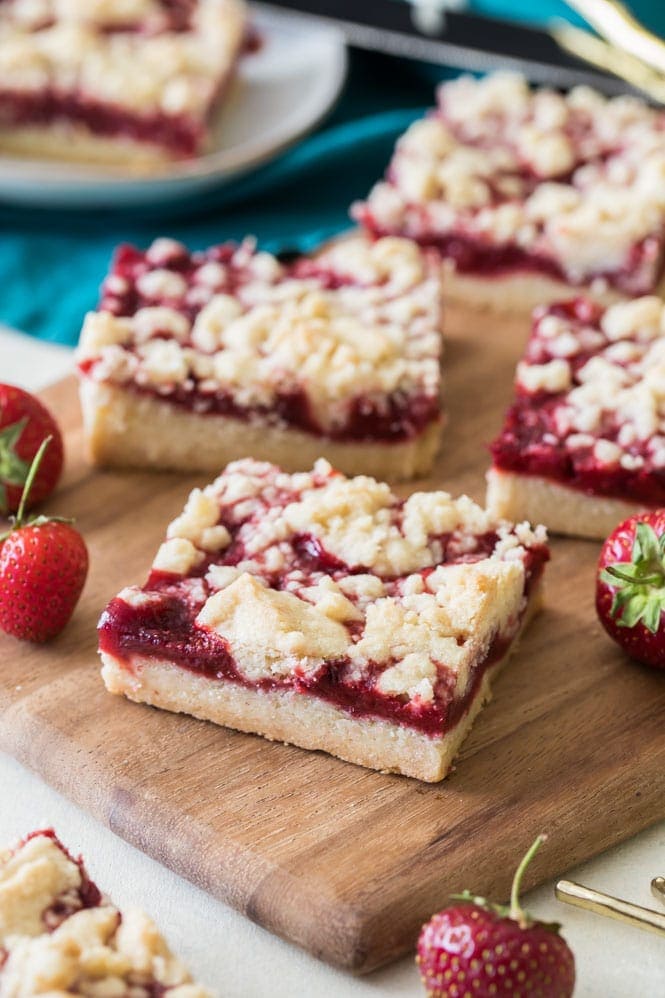 Strawberry Crumb Bars! Refreshing buttery bars with a bright homemade strawberry jam filling. #sugarspunrun #strawberrybars #strawberrydessert #strawberrydessert Strawberry crumb bars on wood cutting board
