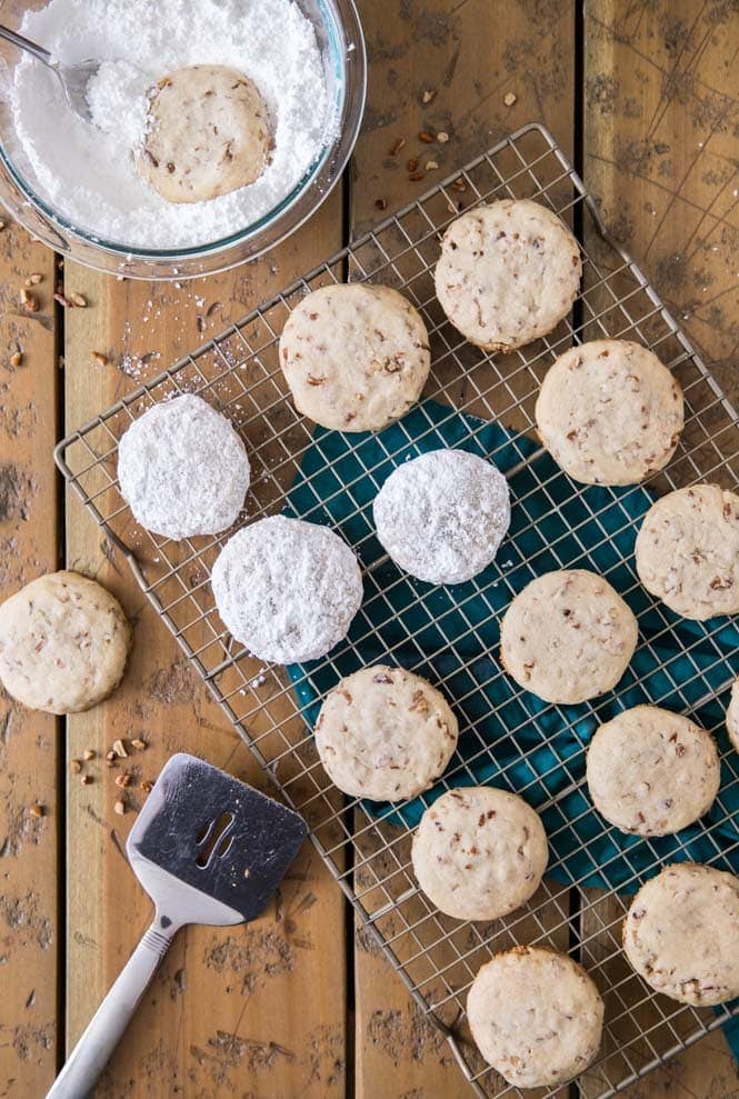 PECAN SANDIES are a simple cookie recipe any time of the year! No chilling and just a few ingredients! #cookierecipe #christmascookie #pecansandies #sugarspunrun Pecan sandies on cooling rack, some being tossed in powdered sugar