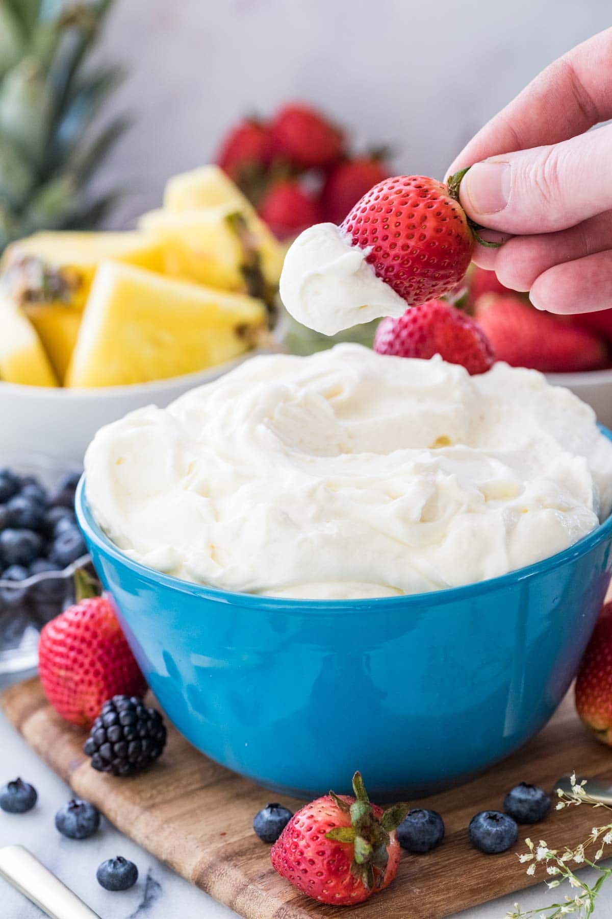 Strawberry being dipped in fruit dip surrounded by other fruit.