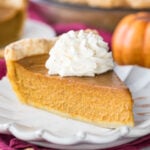 slice of homemade pumpkin pie topped with whipped cream on white plate
