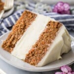 slice of carrot cake cheesecake frosted with cream cheese icing on a white plate