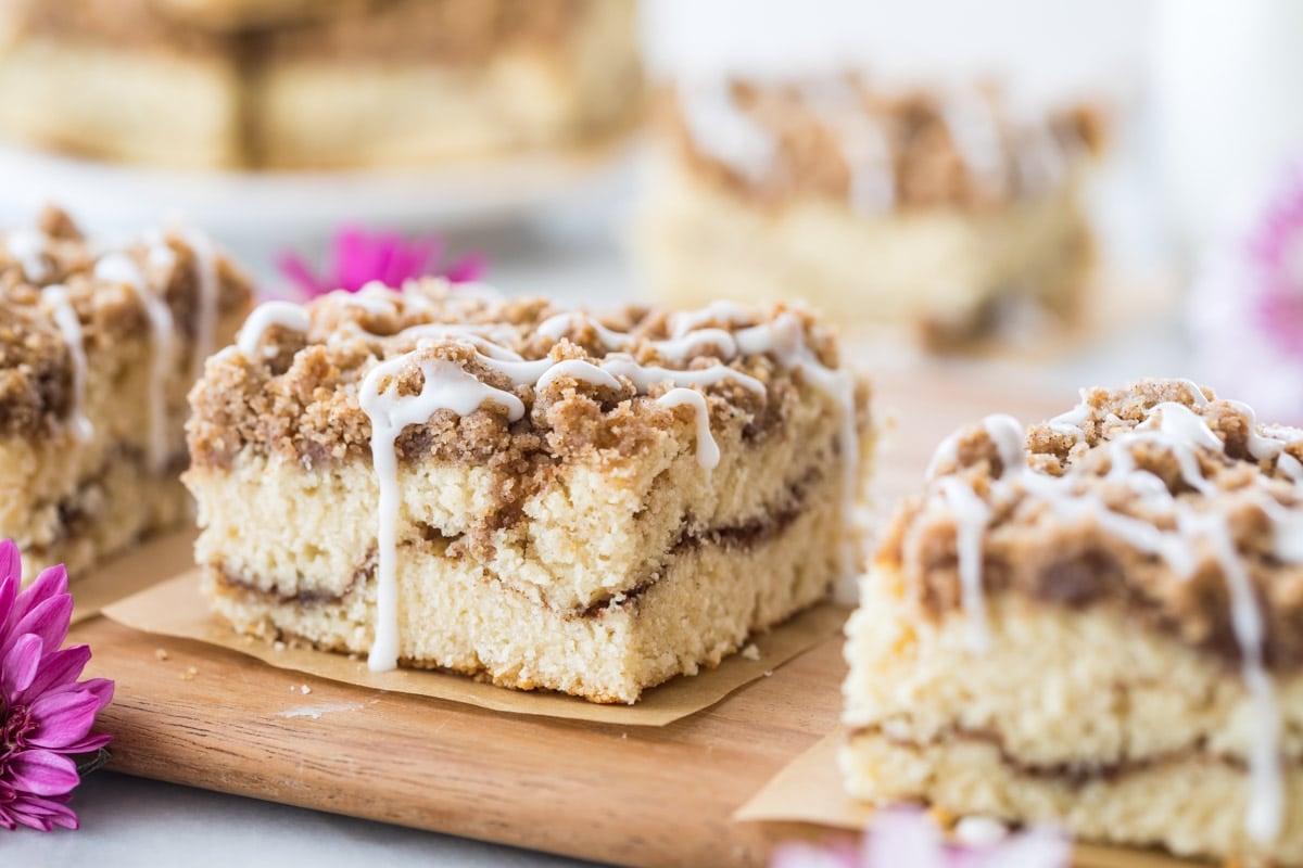 square slices of cinnamon coffee cake with a crumb topping, cinnamon swirl middle, and vanilla drizzle dripping off the side.