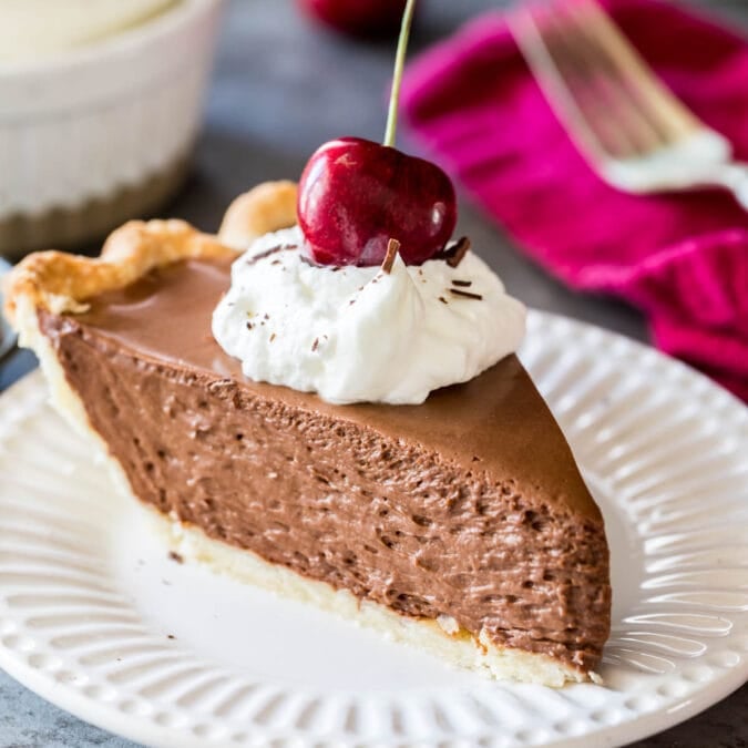 Slice of French silk pie topped with whipped cream and a sweet cherry served on a white plate.