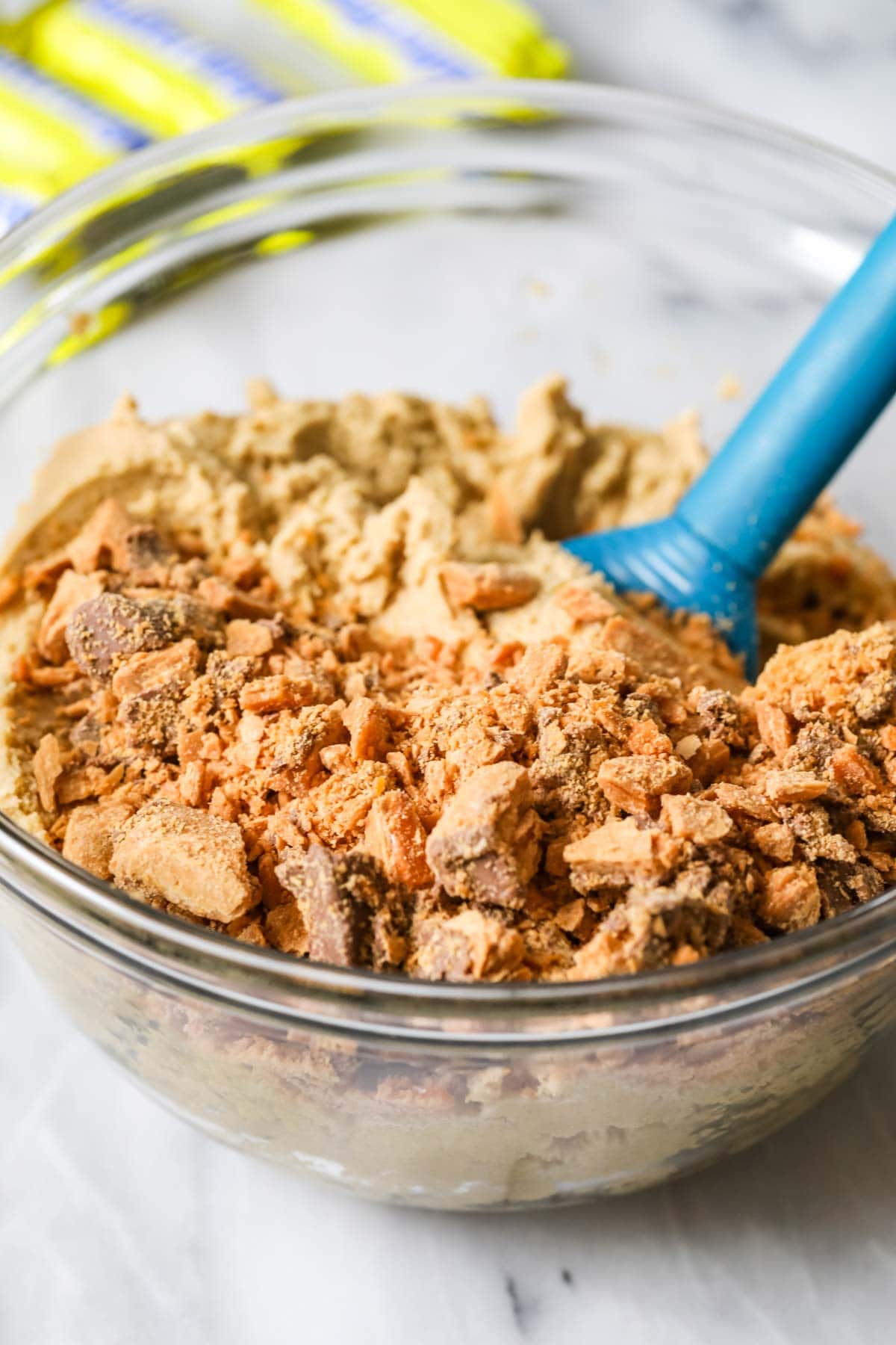 Clear glass bowl of cookie dough with crushed butterfinger candies sprinkled on top.