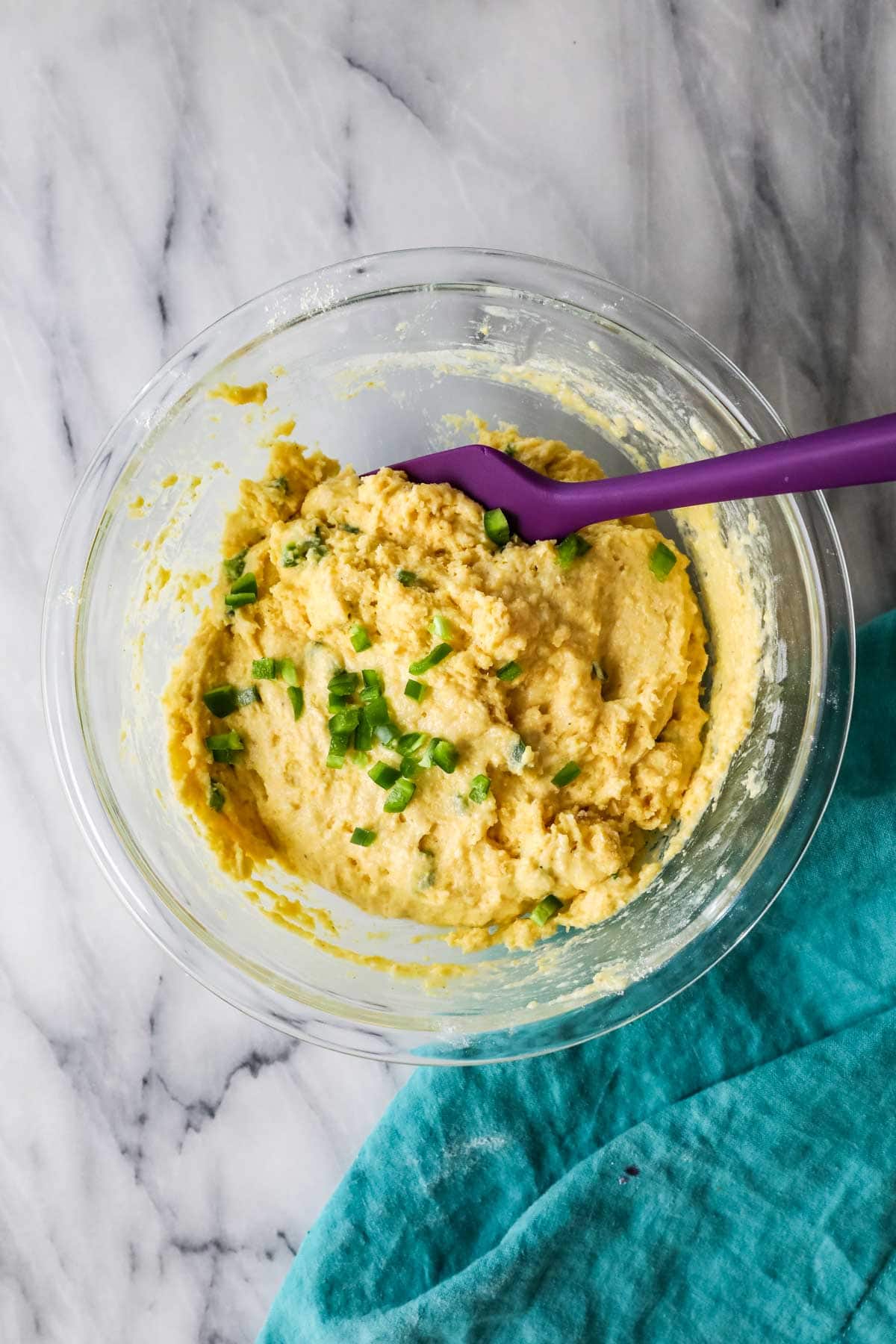 Overhead view of a bowl of cornbread batter with chopped jalapenos being stirred into it.