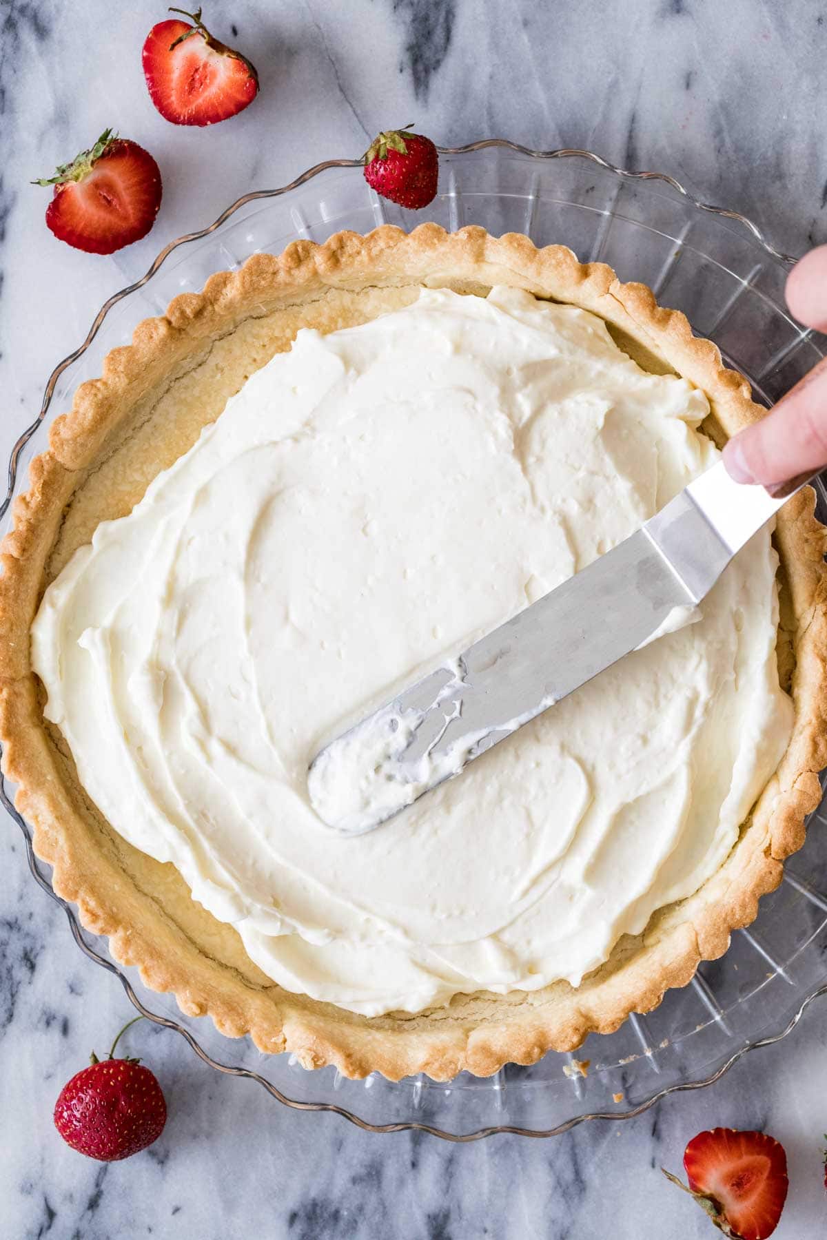 Overhead view of a cream cheese filling being smoothed into a tart crust with an offset spatula.