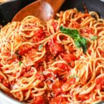 Pasta with arrabiata sauce being stirred by a wood spoon.