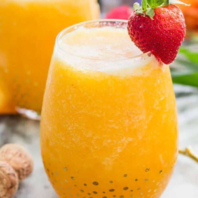 Frozen peach bellini in a glass with a strawberry garnish.