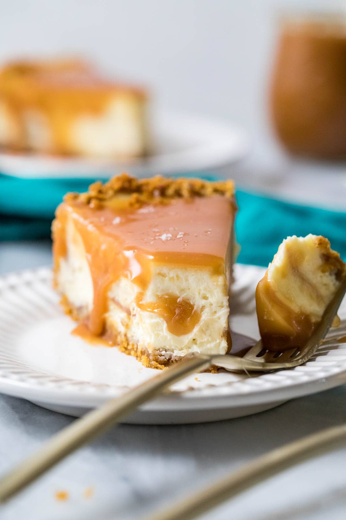 Fork with a bite of caramel cheesecake on a plate beside the slice.