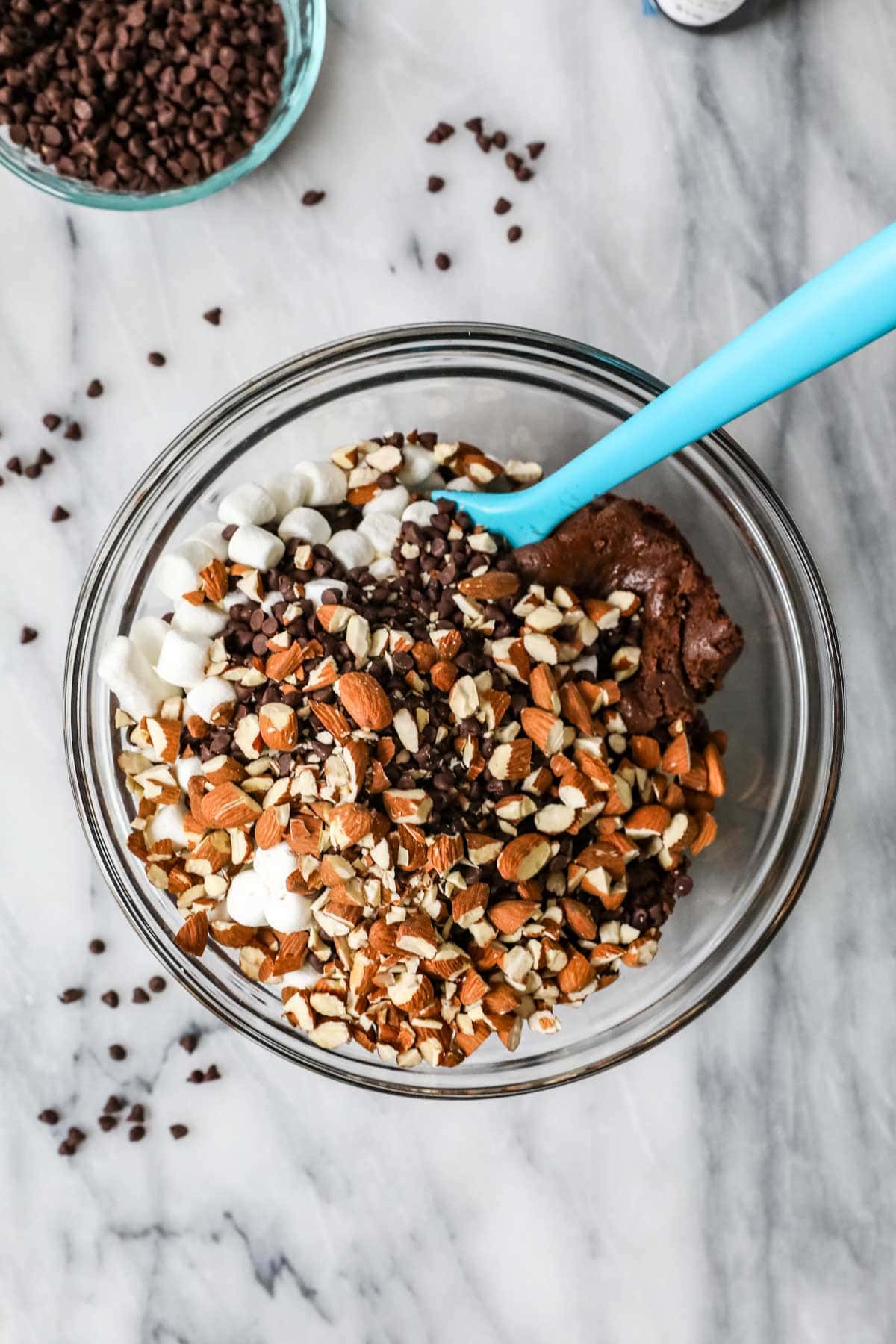 Overhead view of a bowl of chocolate cookie dough with mini marshmallows, mini chocolate chips, and broken almond pieces on top.
