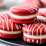Three red velvet macarons stacked in a pyramid shape with more macarons behind.
