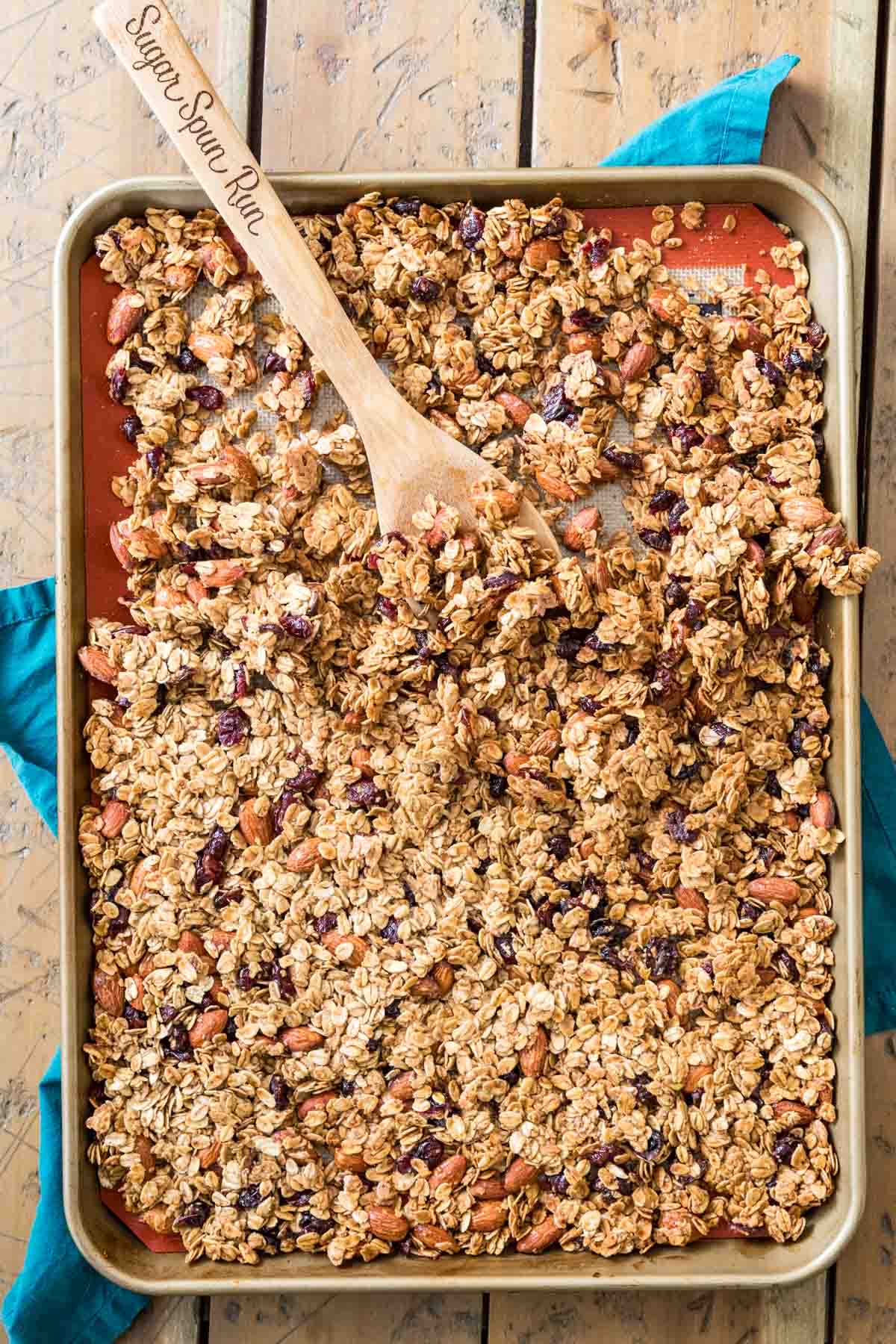 Overhead view of cooked granola on pan, halfway broken up with wooden spoon