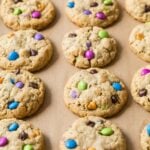 Rows of monster cookies made with colorful candies on a baking sheet.