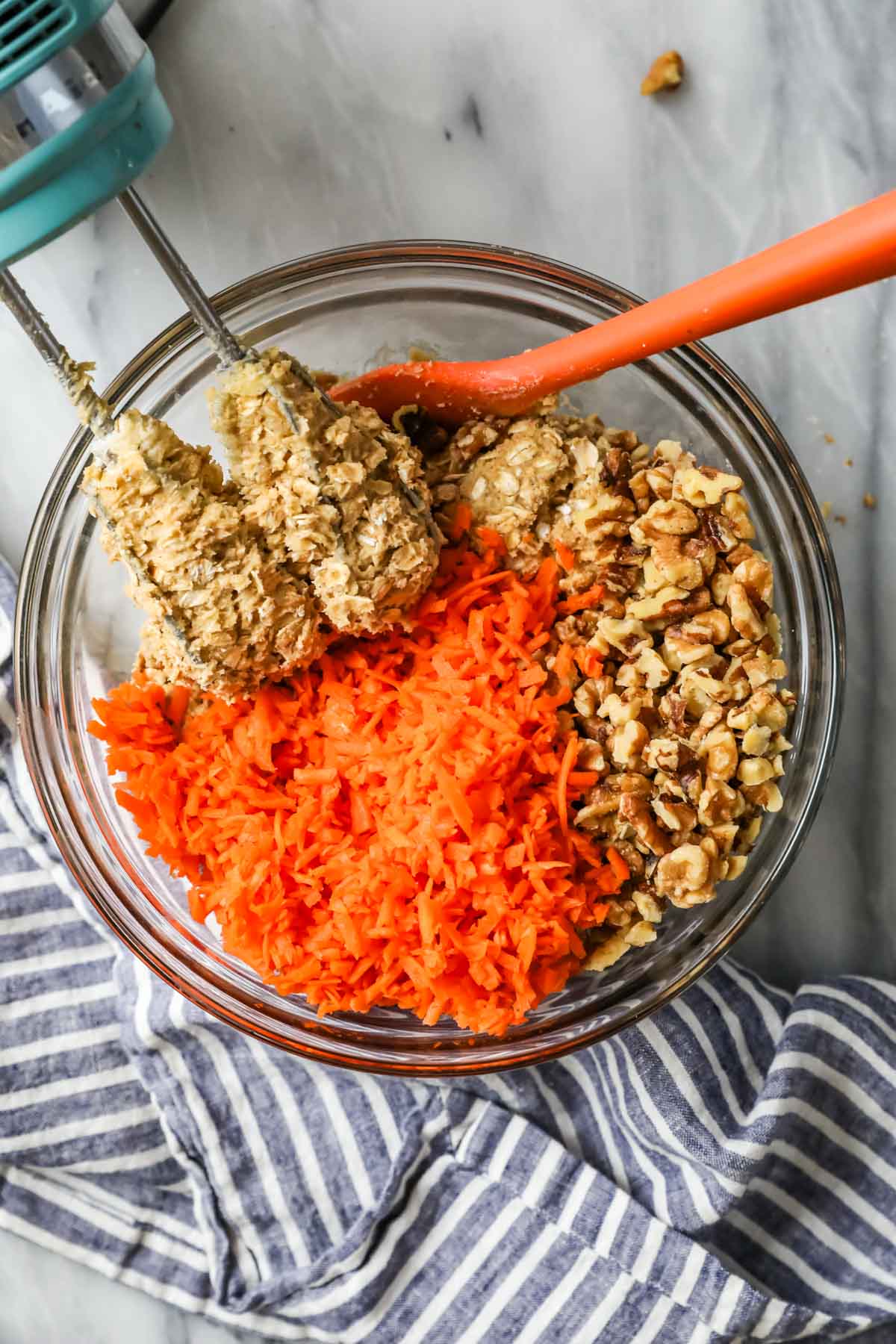 Overhead view of a bowl of oatmeal cookie dough with shredded carrots and pecans poured on top.