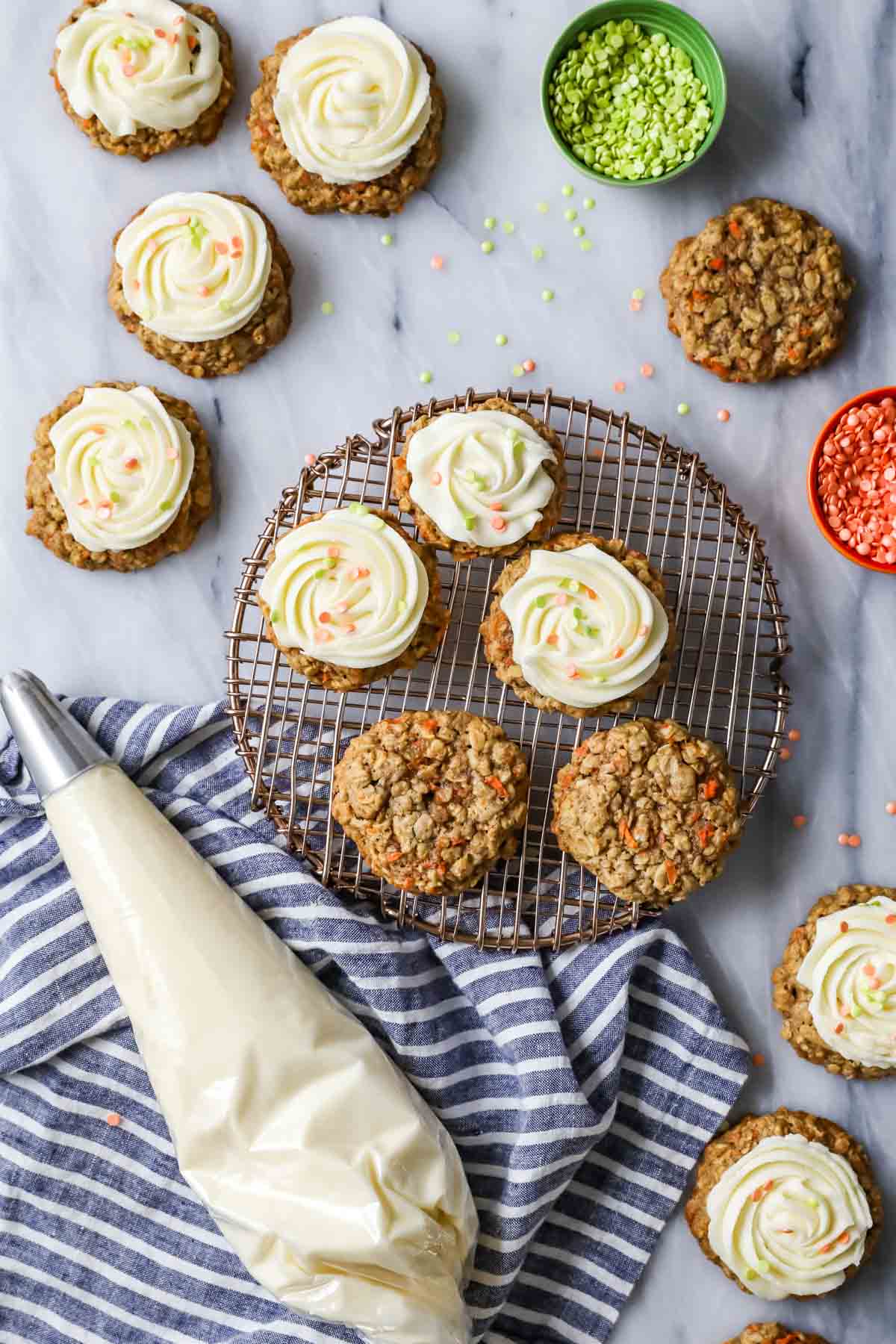 Overhead view of carrot cake cookies on a cooling rack beside a piping bag of cream cheese frosting.