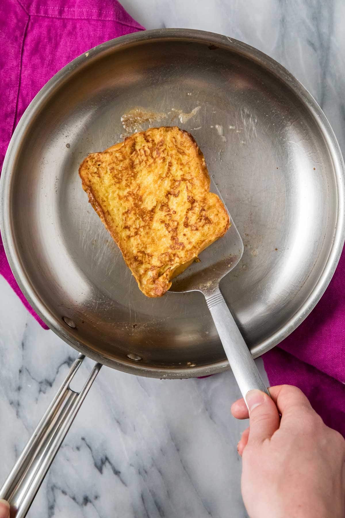 Overhead view of a slice of brioche bread being flipped in a pan.