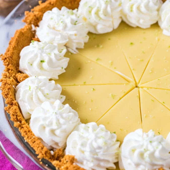 Key lime pie that's been cut into slices and topped with whipped cream swirls.