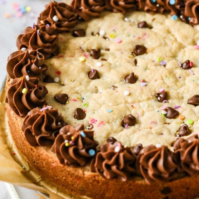 Close-up view of a chocolate chip cookie cake topped with a ring of chocolate frosting and sprinkles.