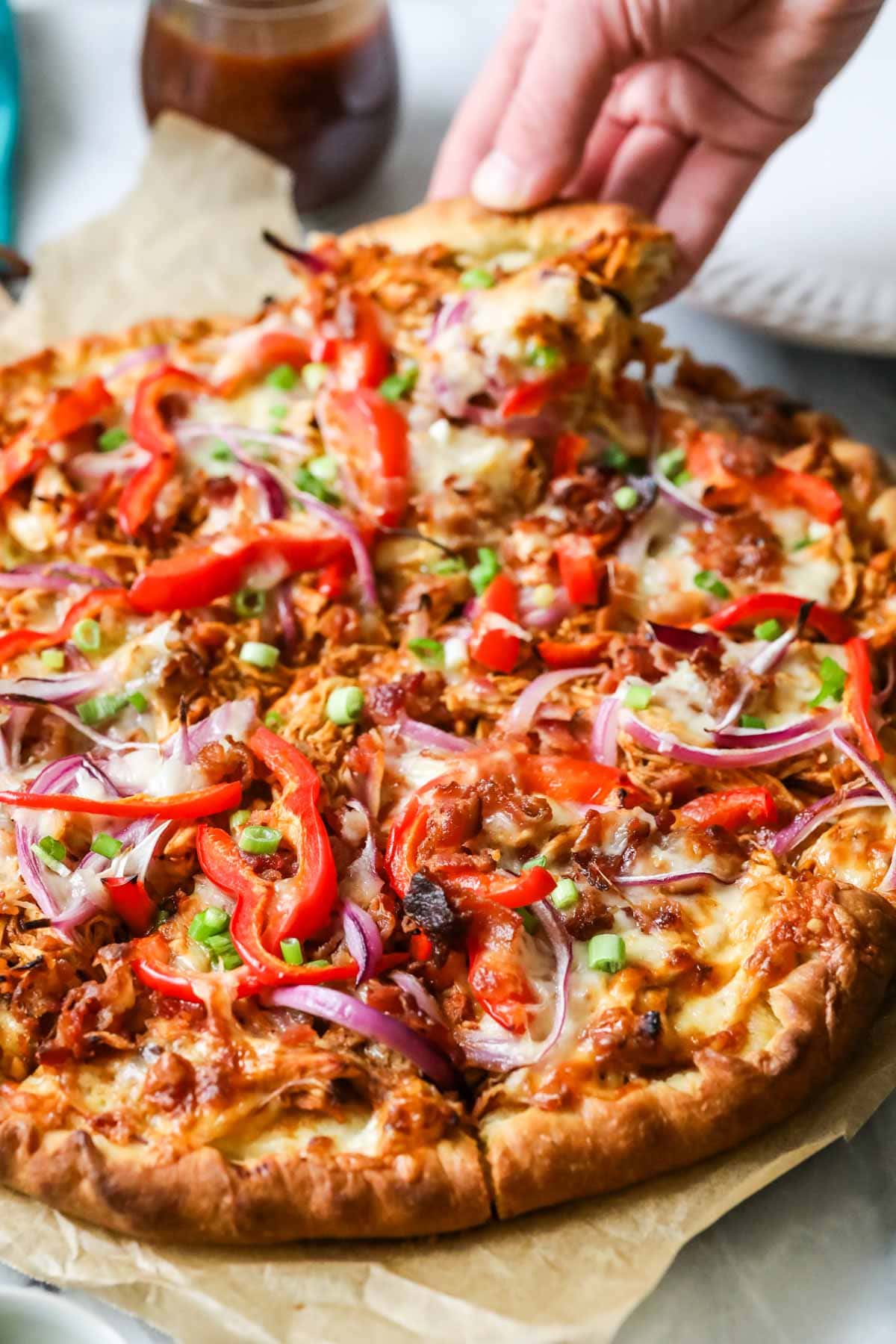 Slice being pulled from a pizza made with BBQ chicken, peppers, onions, and more.
