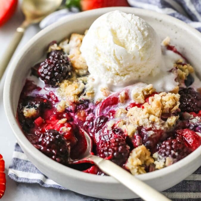 Bowl of berry crisp topped with a melting scoop of vanilla ice cream.