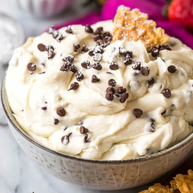 Bowl of cannoli dip topped with mini chocolate chips and a pizzelle cookie.