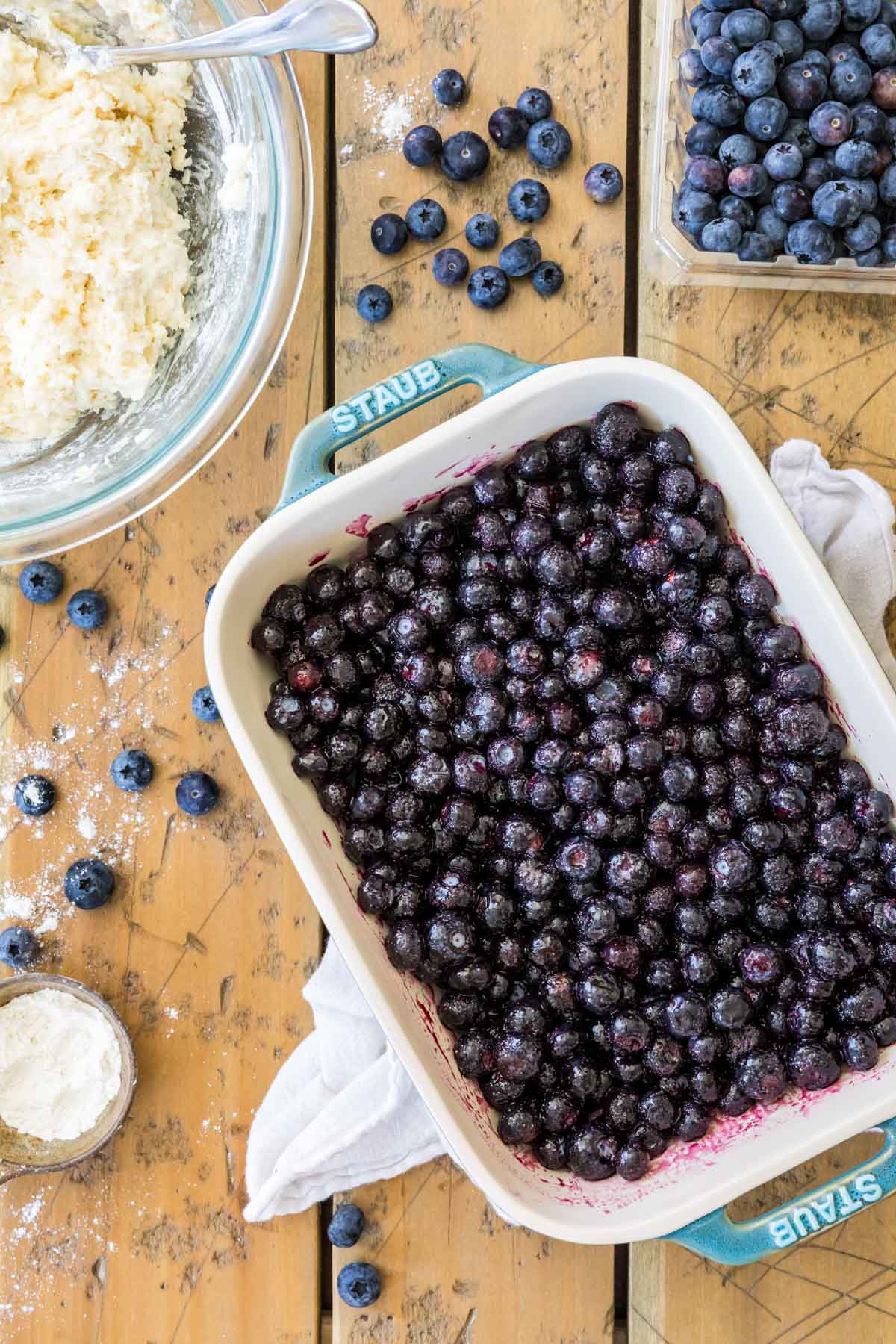 Overhead view of a baking pan of blueberries next to a bowl of cobbler dough.