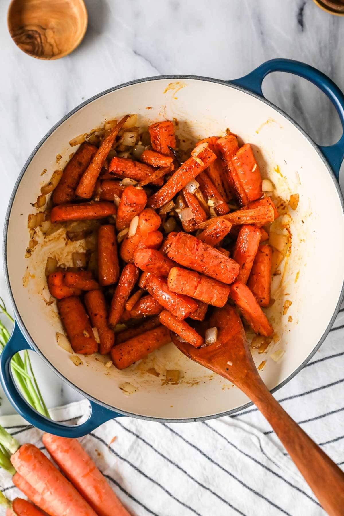 Roasted carrots being added to a dutch oven with onions and spices.