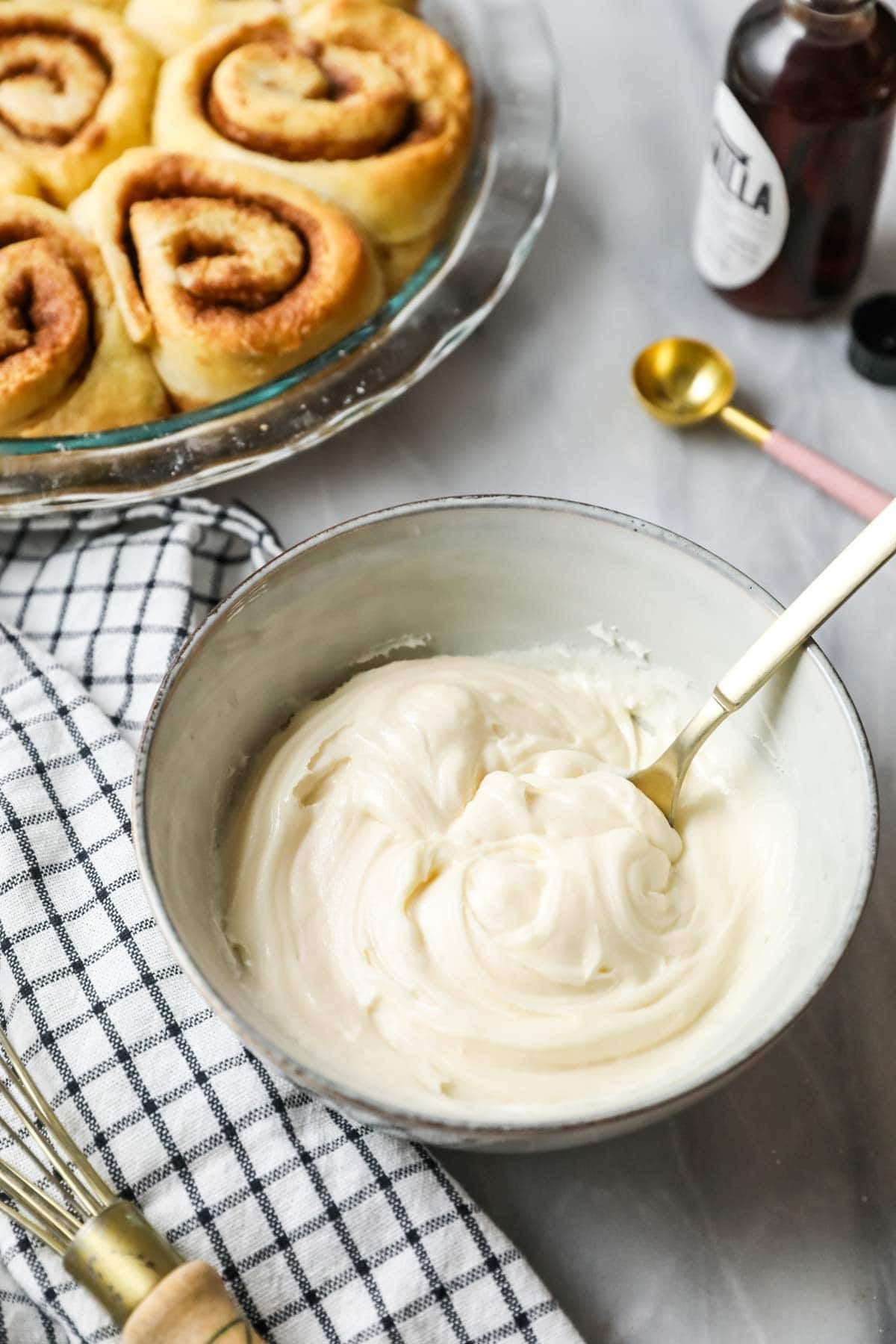 Overhead view of a bowl of icing beside a pan of unfrosted cinnamon rolls.