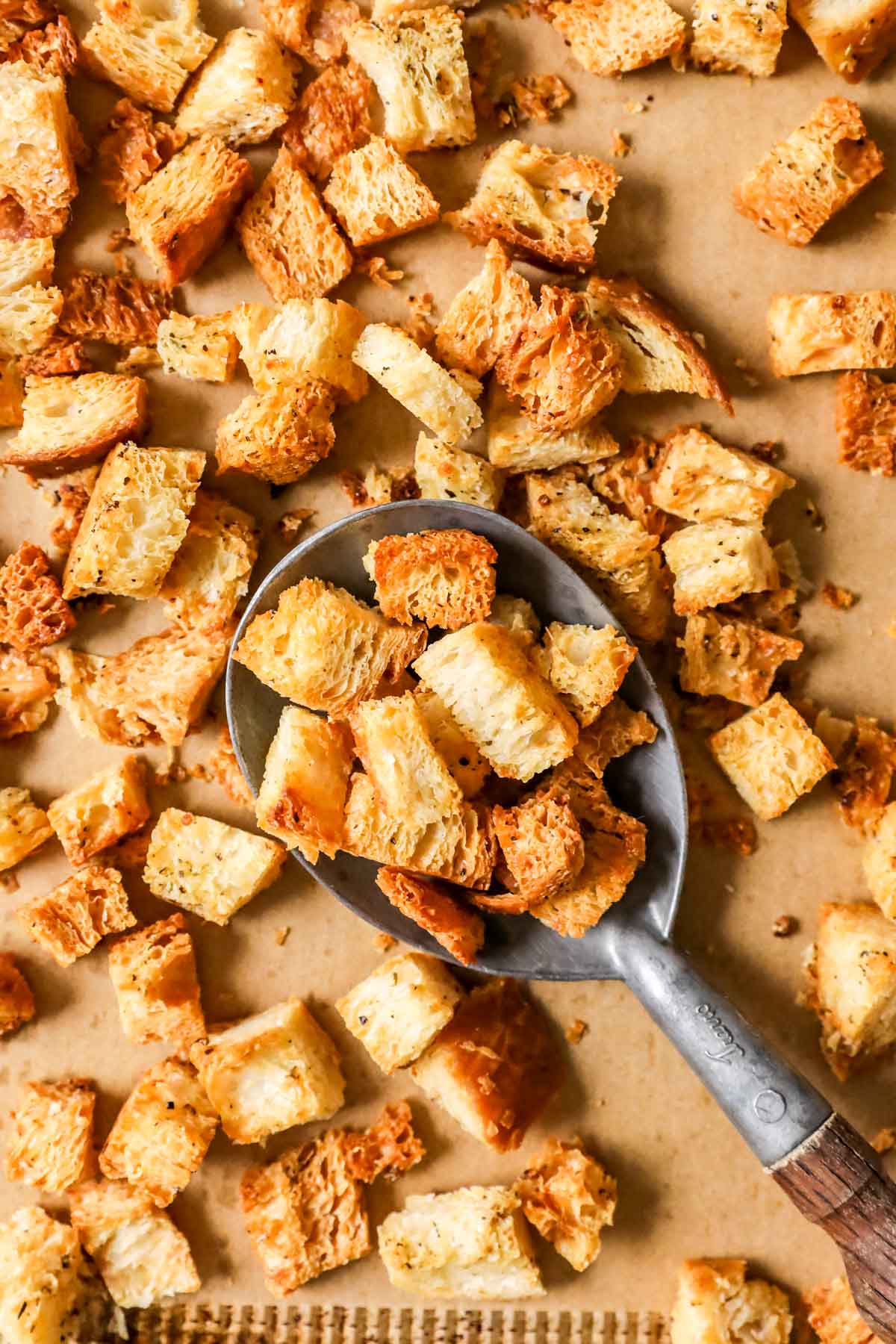 Overhead view of golden brown homemade croutons being scooped off a a baking sheet.