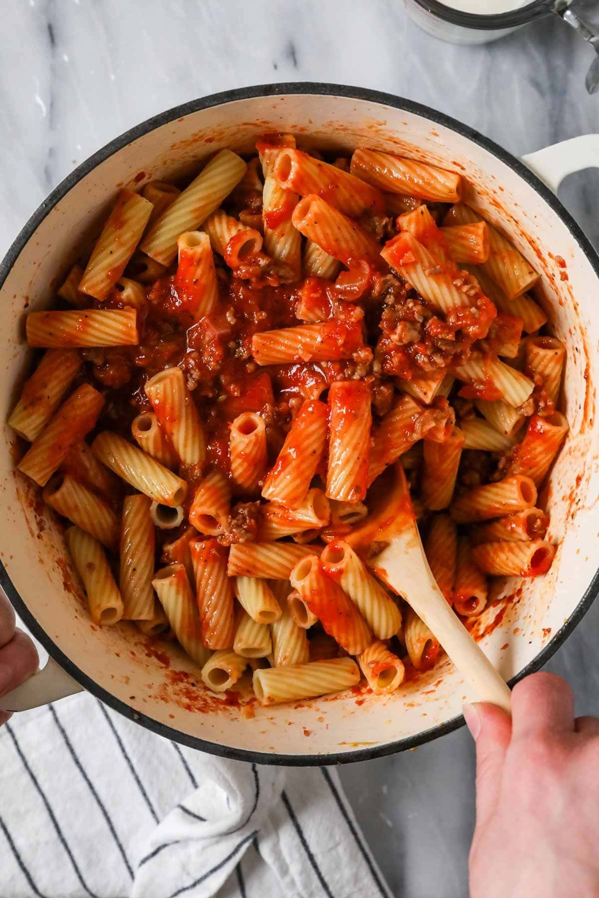 Rigatoni noodles being tossed in a tomato and sausage sauce.