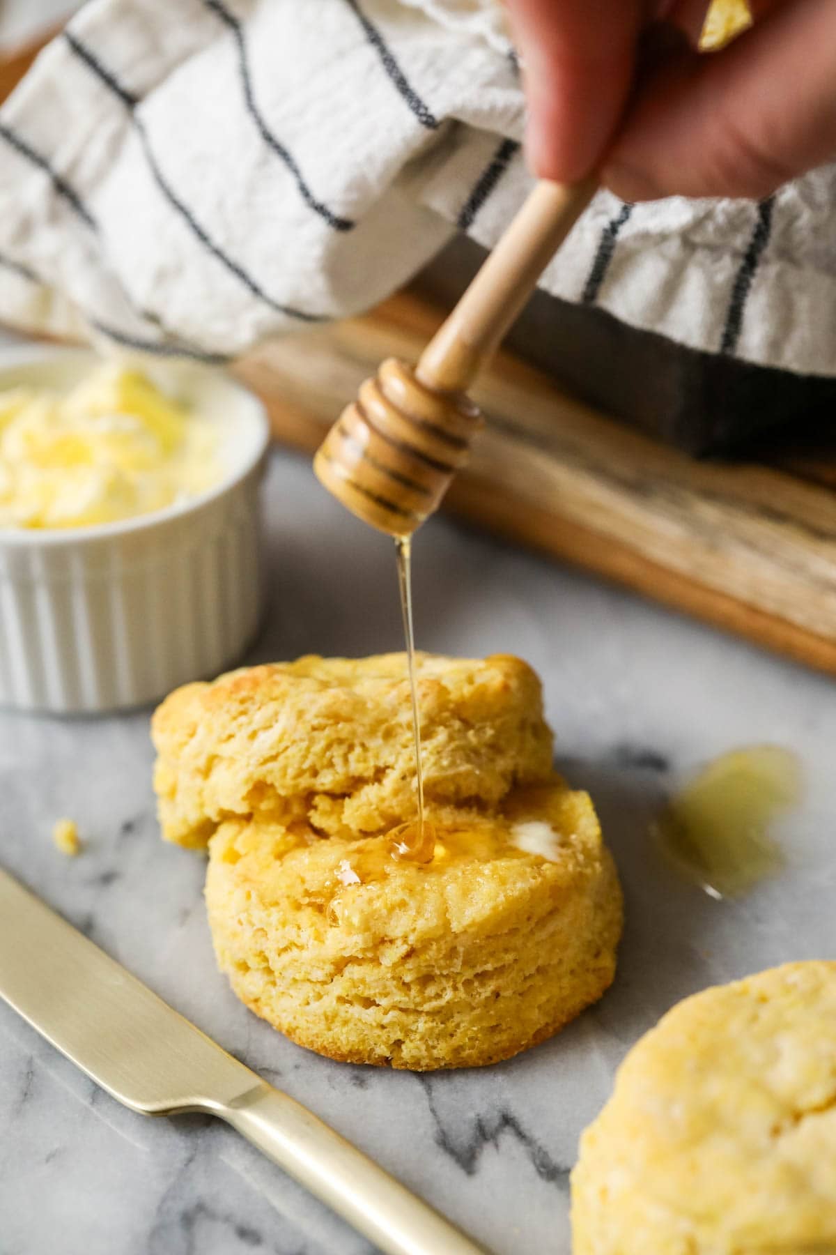 Honey being drizzled over a buttered cornbread biscuit.