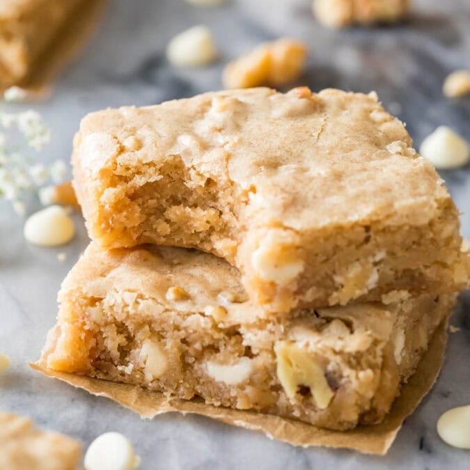 Two blondies from my blondie recipe, stacked on top each other, one with a bite missing to show the chewy center