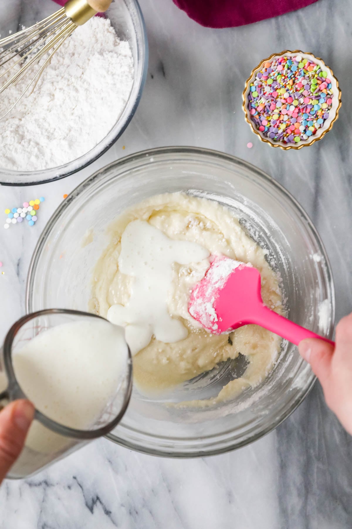 Overhead view of buttermilk being poured into a cupcake batter.
