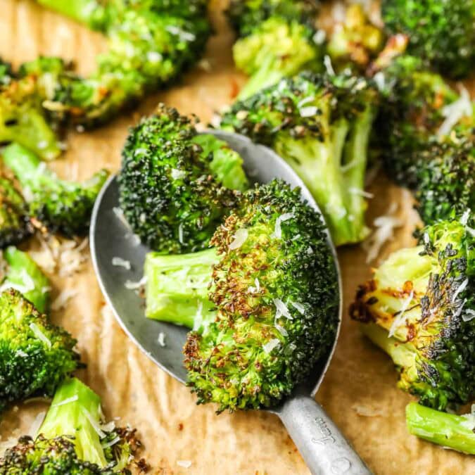 Spoonful of roasted broccoli being scooped off a baking sheet.