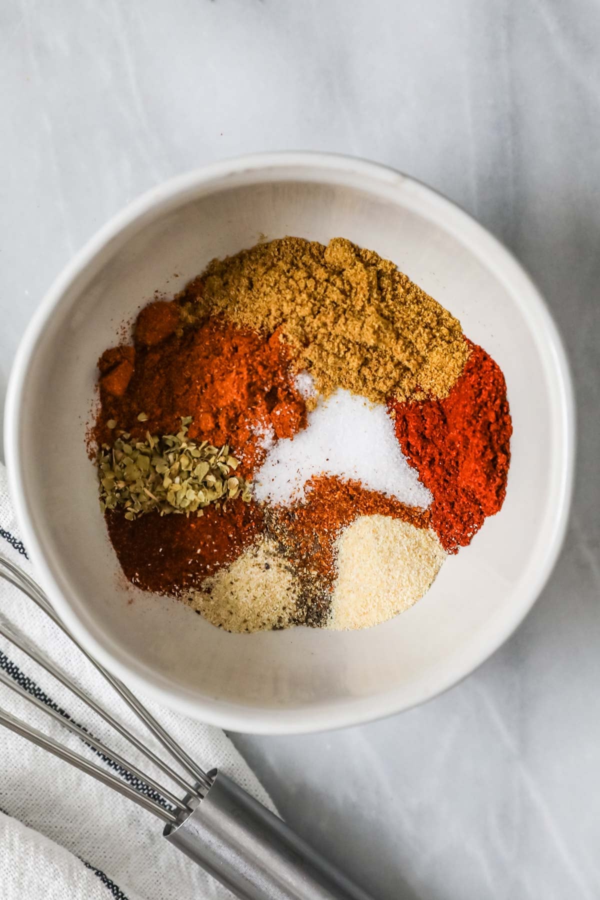 Overhead view of a bowl of spices including cumin, garlic powder, chili powder, and more.