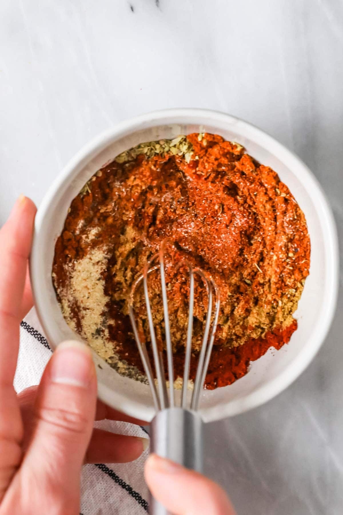 Overhead view of of a whisk combining spices for a homemade taco seasoning recipe.