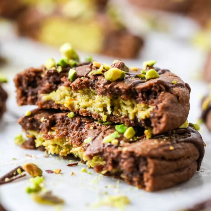 Two stacked halves of a Dubai chocolate cookie filled with pistachio cream and kataifi.