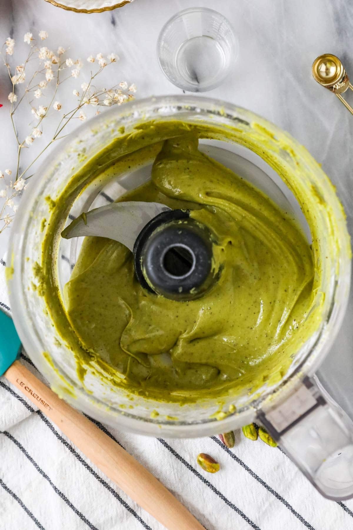 Overhead view of a food processor after blending pistachios, powdered sugar, oil, and salt into a cream.