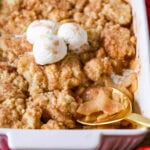 Spoon scooping a serving of apple cobbler from a baking dish.