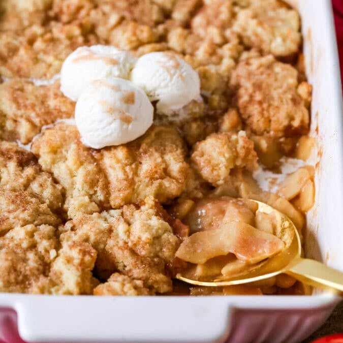 Spoon scooping a serving of apple cobbler from a baking dish.