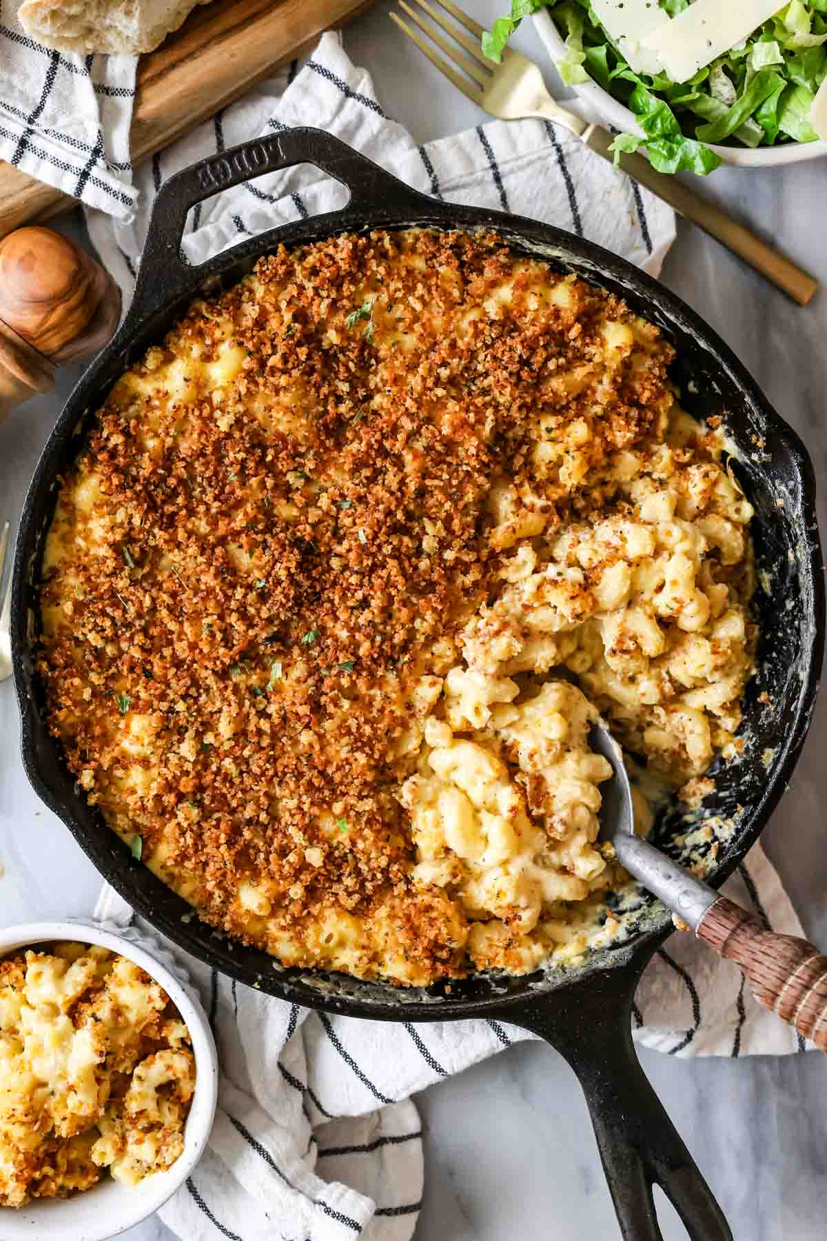 Overhead view of baked mac and cheese in a cast iron skillet -- serving spoon showing cheesy macaroni beneath crisp panko topping.